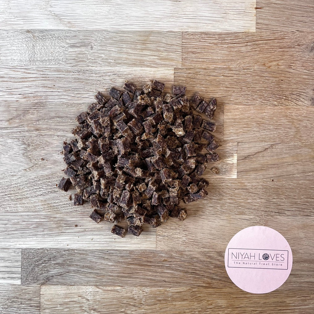 A pile of venison training treats on a wooden surface, with a round label in the lower right corner showing the brand 'NIYAH LOVES'.
